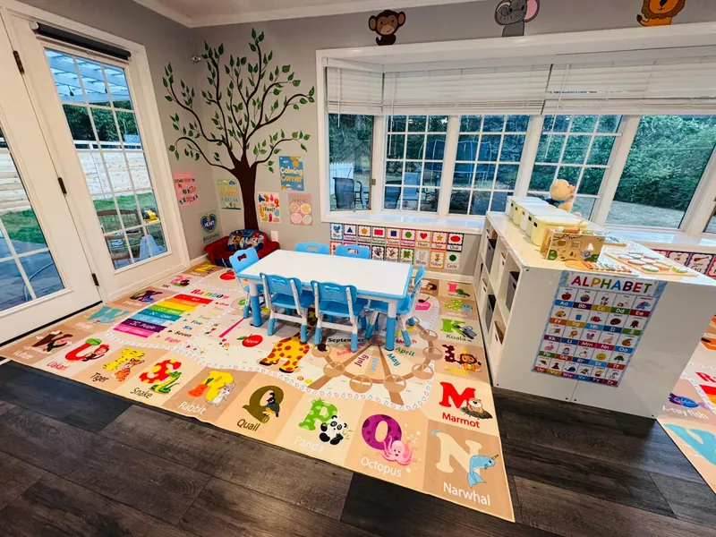 Learning area with educational floor mat, blue table and chairs, tree mural, and natural lighting